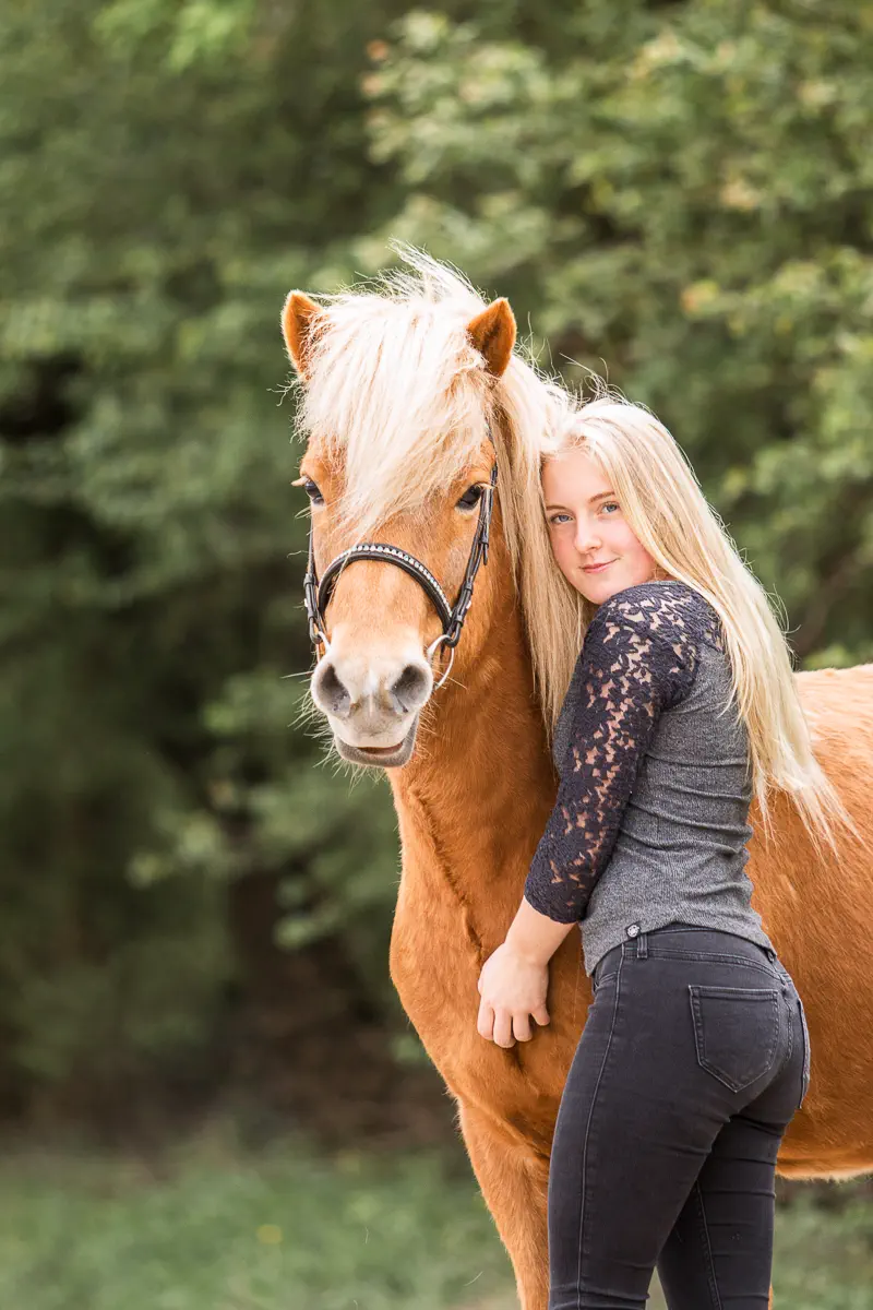 Mädchen steht neben ihrem fuchsfarbenen Islandpferd und umarmt es im Portrait